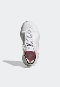 White athletic shoe with a textured upper, pink accents, and a ridged sole. Features a lace-up design and a branded insole.