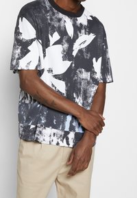 Krótki rękaw t-shirt w czarno-białym kolorze z kwiatowym wzorem, z okrągłym dekoltem i luźnym krojem. Wykonany z miękkiego, lekko teksturowanego materiału.