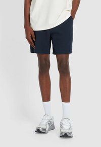 Dunkelblaue Shorts mit Struktur in einer entspannten Passform, kombiniert mit weißen Sportsocken und silbergrauen Laufschuhen mit reflektierenden Akzenten.
