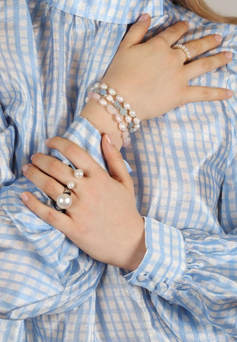 Silver ring med tre pärlor, staplad armband av pärlor och färgglada ädelstenar, ljusblå och vit randig satinblus med puffärmar.