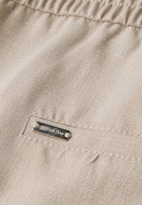 Beige tyg med en fin texturering, som har ett elastiskt midjeband och en liten silvertagg som säger "Street One."