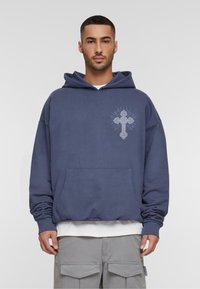 Marineblauwe hoodie van zacht materiaal, met een voorzak en een decoratieve lichtgrijze kruisgrafiek op de linkerborst.