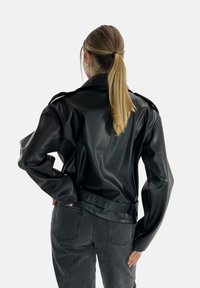 Svart konstläderjacka med strukturerade axlar, knäppta epåletter och en kort passform. Matchad med högmidjade grå jeans.