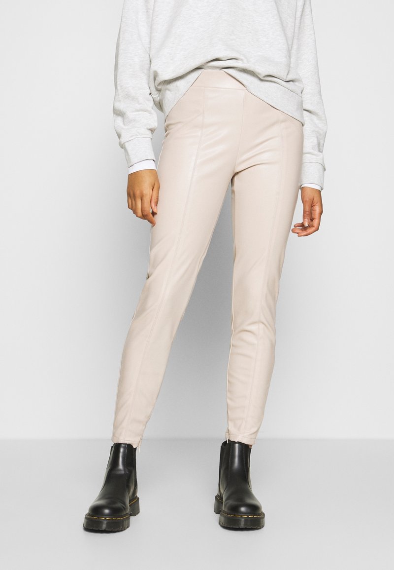 Leggings in finta pelle beige con una vestibilità slim, caratterizzati da dettagli cuciti e una vita elastica, abbinati a stivali neri alla caviglia.