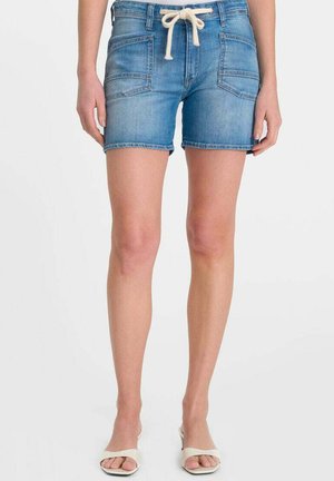 Persoon draagt middenblauwe denimshorts met voorzakken en een witte trekkoord, gecombineerd met witte open-teen sandalen.