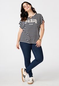 Gestreept T-shirt in marineblauw en crème met de tekst "PARIS FRANCE", gecombineerd met donkerblauwe jeans en witte sneakers met zwarte accenten.