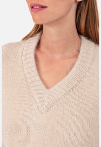 Beiger Strickpullover mit tiefem V-Ausschnitt, mit geripptem Muster am Kragen und Körper, weiches, leichtes Material.