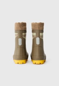 Botas de goma marrones con un puño de tela marrón texturizada, suelas amarillas y acentos reflectantes en los lados. Presentan un diseño elegante y moderno.