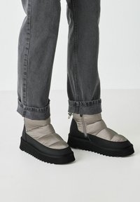 Stivali alla caviglia in stile puff argento e nero, caratterizzati da un design imbottito, suola in gomma spessa e dettagli con zip sul lato.