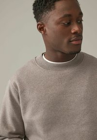 Sudadera gris con tejido texturizado, cuello acanalado y diseño de cuello redondo. Apariencia suave, ajustada sin adornos.