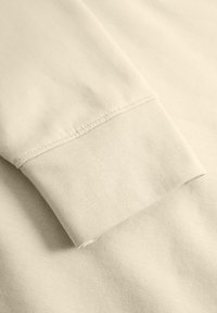 Lichtbeige katoenen sweatshirtmanchetten tonen een ribbeltextuur met nette stiksels. Zachte stof met een gladde afwerking, omgeslagen aan de rand.