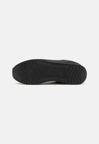 Black sneaker sole with textured rubber for traction, featuring zigzag patterns and raised accents, branded with "BOSS" on the side.