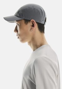 Grey cap with perforated design on the sides and a flat brim, paired with a light-colored, textured athletic shirt.