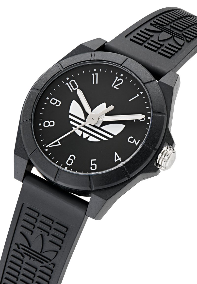 Montre analogique noire avec un cadran rond, des chiffres arabes blancs, des aiguilles argentées, un bracelet en caoutchouc noir avec un motif de logo et une finition texturée.