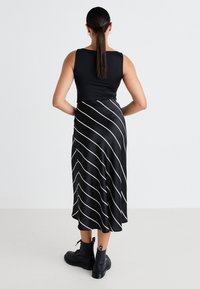 Svart tanktopp kombinert med et svart skjørt med hvite diagonale striper. Utseendet kompletteres av svarte snørebots.