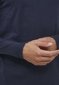 Morska plava košulja dugih rukava izrađena od glatkog materijala, s prilagođenim dizajnom jednostavnog šavljenja i okruglim izrezom.