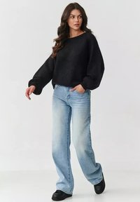 Czarny dziany sweter z bufiastymi rękawami, zestawiony z jasnoniebieskimi spodniami z szerokimi nogawkami i czarnymi butami, na jednolitym białym tle.