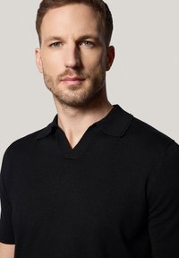Czarna, krótko rękawowa koszulka polo z dekoltem w kształcie litery V i miękką, dzianinową teksturą, z klasycznym kołnierzem i minimalnymi detalami.