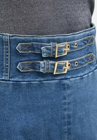 Jeansskørt med to guldspænder og detaljeret syning. Har en tætsiddende talje og en glat tekstur i en mellemblå farve.