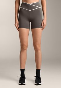 Sive atletske kratke hlače z visokim, prešitvenim pasom. Gladka tekstura, dolžina do sredine stegna, v kombinaciji s črnimi športnimi copati in kratkimi nogavicami.