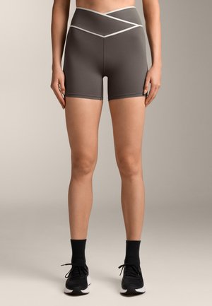 Sivé športové šortky s vysokým pásom s krížovým stehom. Hladká textúra, dĺžka do polovice stehien, v kombinácii s čiernymi teniskami a krátkymi ponožkami.