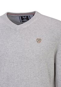 Grijze trui met V-hals en een gestructureerde brei. Heeft een klein schildvormig logo op de linkerborst. Label zichtbaar aan de binnenkant van de kraag.