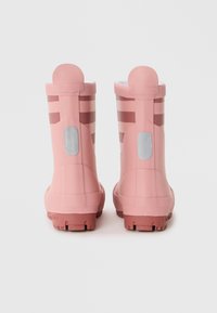 Botas de goma rosas con una textura suave, que presentan rayas horizontales y un tirador redondo en la parte posterior. Suelas gruesas y con patrón para mayor tracción.