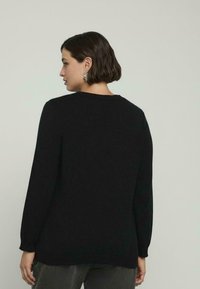 Maglione nero in maglia con maniche lunghe e scollatura rotonda, caratterizzato da una vestibilità rilassata e una texture a coste all'orlo e ai polsini.