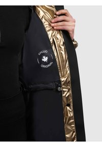 Schwarze Jacke mit glänzendem goldfarbenem Innenfutter, ausgestattet mit einem Logopatch und einem Kordelzugdetail an der Taille. Glatte Textur und sichtbare Kapuze.