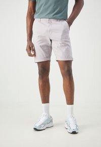 Shorts en jean gris clair avec des revers, poches latérales et passants de ceinture, associés à un t-shirt teal et des baskets avec des accents bleus.