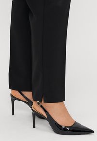 Schwarze Patentanleder Slingback-Absätze mit spitzem Zehenbereich und dünnem Stiletto-Absatz. Verfügt über eine goldfarbene Hardware-Akzentuierung am Riemen.