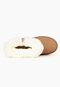 Zapatilla de ante marrón con forro de piel blanca, diseño de parte superior abierta, punta redondeada y borde cosido. Textura suave, apariencia sencilla y acogedora.