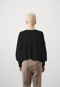 Pulover negru cu dungi, cu un design scurt, decolteu rotund și umeri căzuți, asortat cu pantaloni bej cu talie înaltă.