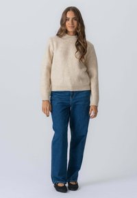 Lys beige strikket sweater med høj hals, parret med blå vidde bukser og sorte flade sko. Tekstureret stof med en afslappet pasform.
