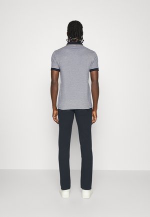 Polo gris avec col et manches navy, associé à un pantalon sombre et des baskets blanches. Conçu pour une coupe décontractée avec une texture lisse.