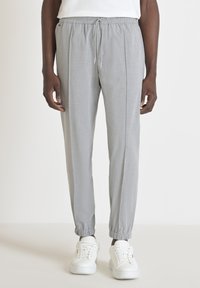 Pantalon de jogging gris clair en tissu lisse, avec une taille élastique et des poignets élastiques, deux poches latérales et une coupe décontractée.