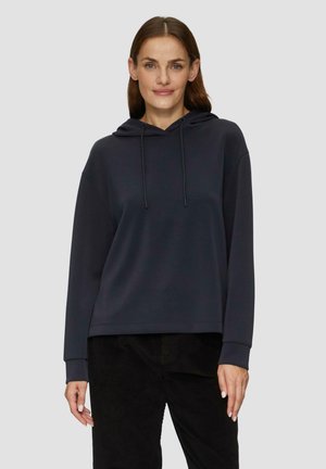 Dunkelgrauer Kapuzenpullover mit langen Ärmeln, Kordelzügen und einem lockeren Schnitt, kombiniert mit schwarzen Cordhosen. Einfaches Design.