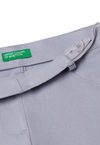 Lichtgrijze denim broek met een knoopsluiting, featuring een groene "United Colors of Benetton" label en een gladde, gestructureerde stof.