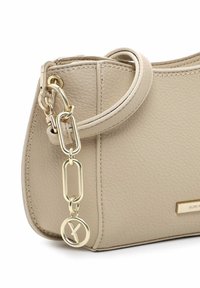 Beige Lederhandtasche mit glatter Oberfläche, geschwungener Form, Hardware in Goldtönen, Kettenakzent und Logoschild an der Seite.