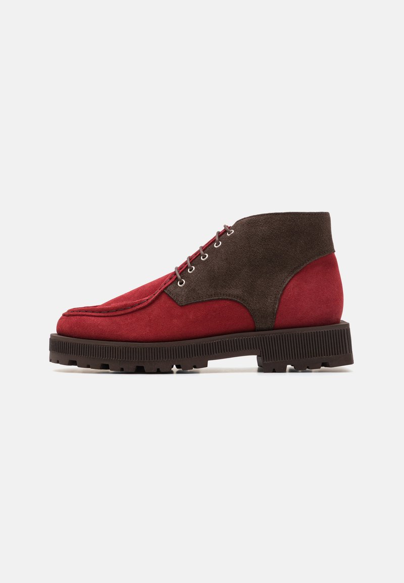 Stivali ankle in camoscio rosso e marrone con punta rotonda, occhielli in metallo e suola in gomma nera testurizzata. Presentano pannelli superiori a contrasto.