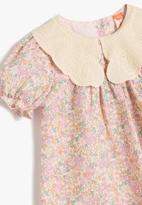 Vestido de bebé floral con tela en tono rosa pastel, un cuello con puntilla en forma de ondas y mangas abullonadas con estampado de flores coloridas.