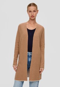 Cardigan long léger couleur brun clair en matière douce, avec un design ouvert à l'avant, rehaussé d'une bordure crème contrastante au niveau des poignets et de l'ourlet. Porté par-dessus un haut sombre.