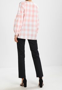 Blusa de cuadros rosa y blanca con mangas abullonadas, combinada con pantalones slim negros y zapatos de tacón negros. Cuello redondo sencillo.