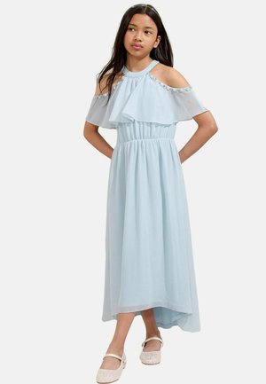 Vestido maxi azul claro con mangas caídas, detalle de volantes en capas, cinturilla elástica y dobladillo asimétrico. Combinado con zapatos planos plateados.