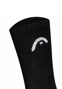 Schwarze, gerippte Socke mit einem weißen, geschwungenen Logo nahe dem oberen Bund auf weißem, einfarbigem Hintergrund.