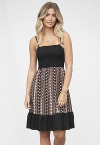 Robe noire avec un corsage smocké et des bretelles fines, avec une jupe à motifs aux tons terreux et un ourlet à volants.