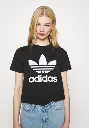 Czarna bawełniana koszulka z krótkim rękawem, z dużym białym logo Adidas i trzema paskami pod stylizowanym wzorem trefoil. Luźny krój.