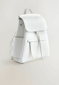 Sac à dos en cuir blanc avec fermeture à rabat, poche avant zippée, cordon de serrage et poches latérales sur fond neutre.