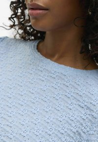 Top azzurro chiaro con texture, caratterizzato da un motivo a pois, scollatura tonda e maniche corte, con un aspetto di tessuto morbido e intrecciato.