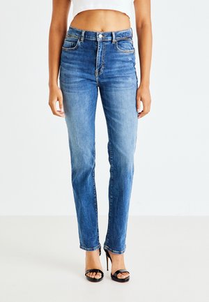 Jean en denim à teinte bleu moyen, taille haute, cinq poches et une texture légèrement usée au niveau des genoux. Conçu avec des passes-belt.